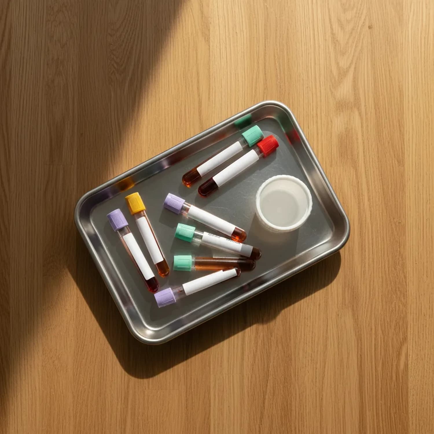 Combo perimenopausia con panel hormonal: bandeja de acero con 7 tubos de extracción y un frasco de orina sobre superficie de roble, luz suave matinal.