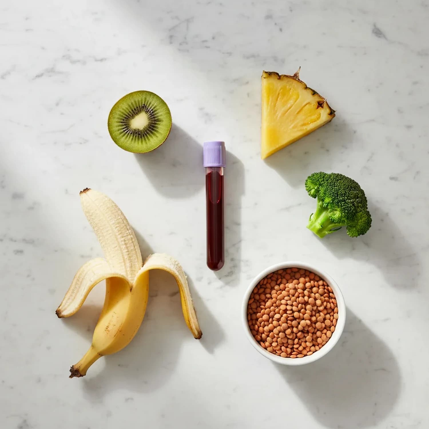 Panel 3 de intolerancia alimentaria IgG: tubo de extracción de sangre junto a kiwi, banana, ananá, brócoli y un cuenco con lentejas, sobre mármol claro.