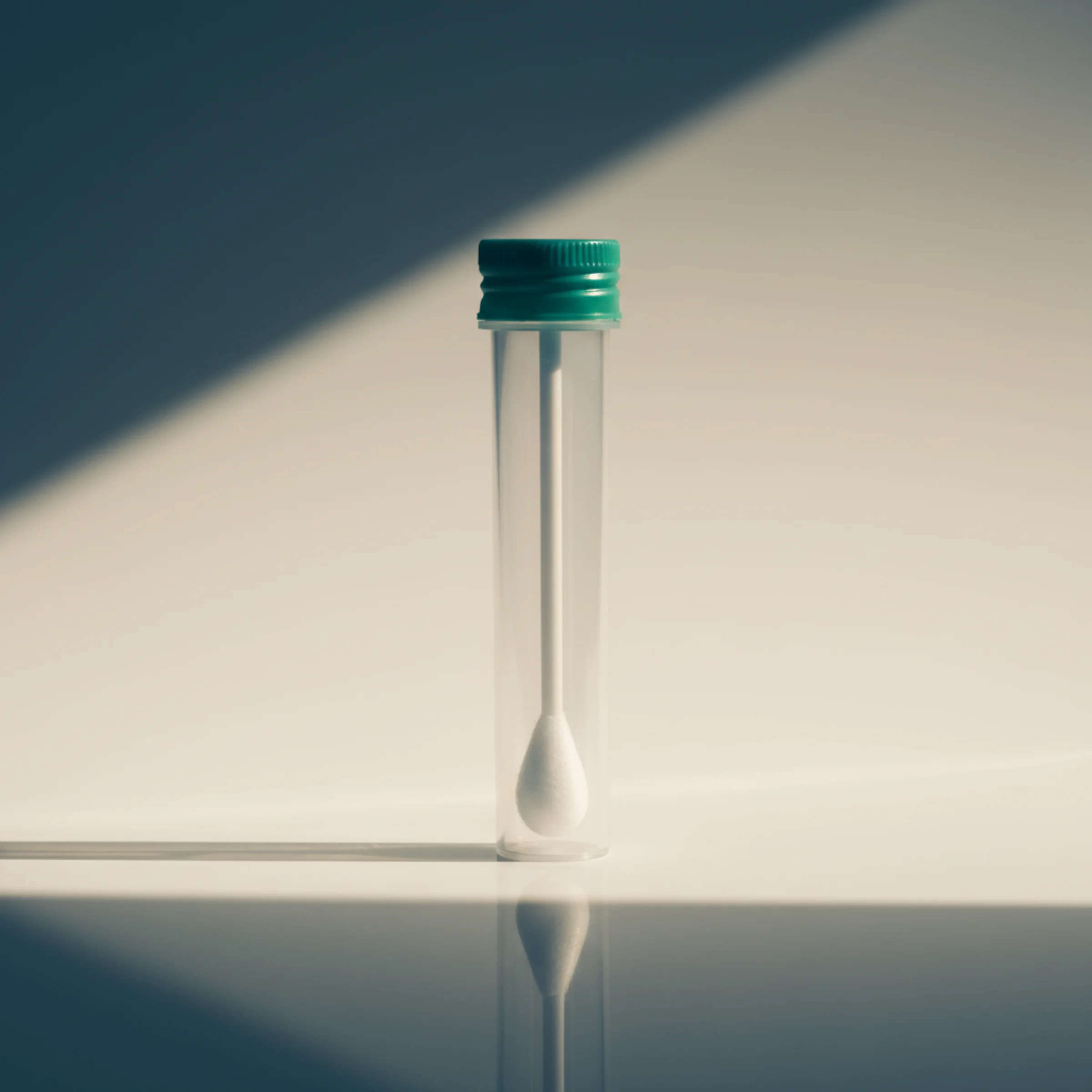 Viruela símica (Mpox) por PCR: tubo de transporte vertical con tapa verde-azulada y un hisopo estéril visible en su interior, iluminación lateral.